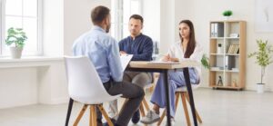 A couple sits across from a professional during a meeting, discussing documents together in a bright office setting.