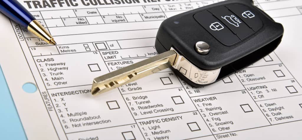 A car key and pen rest on a traffic collision report form, featuring checkboxes and sections for detailed accident information.